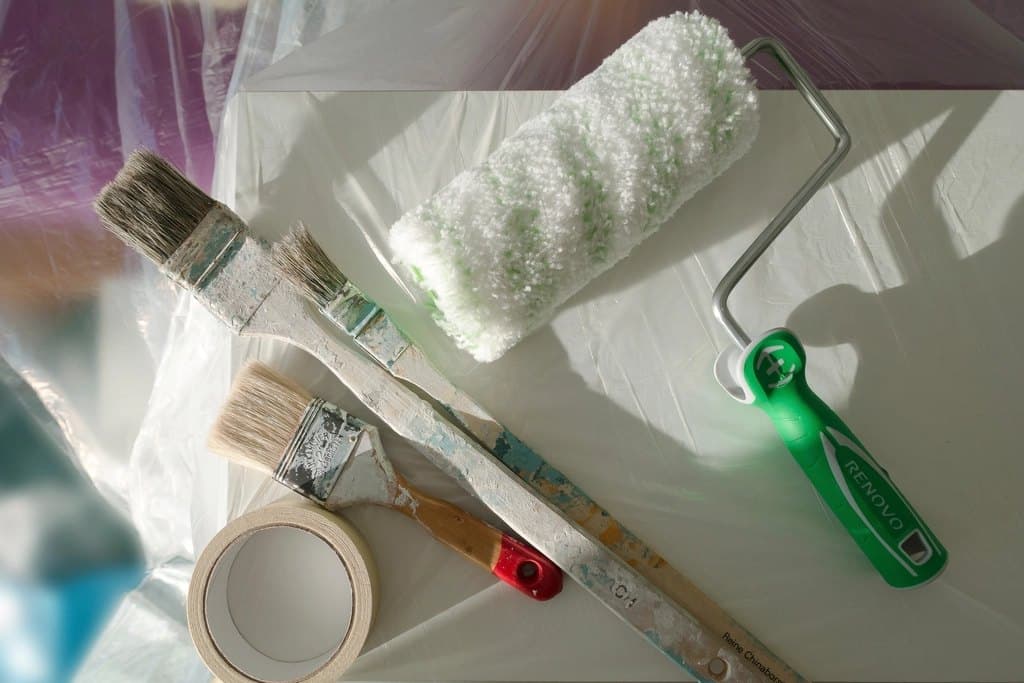Paint roller, brushes and masking tape laid out on a dust sheet