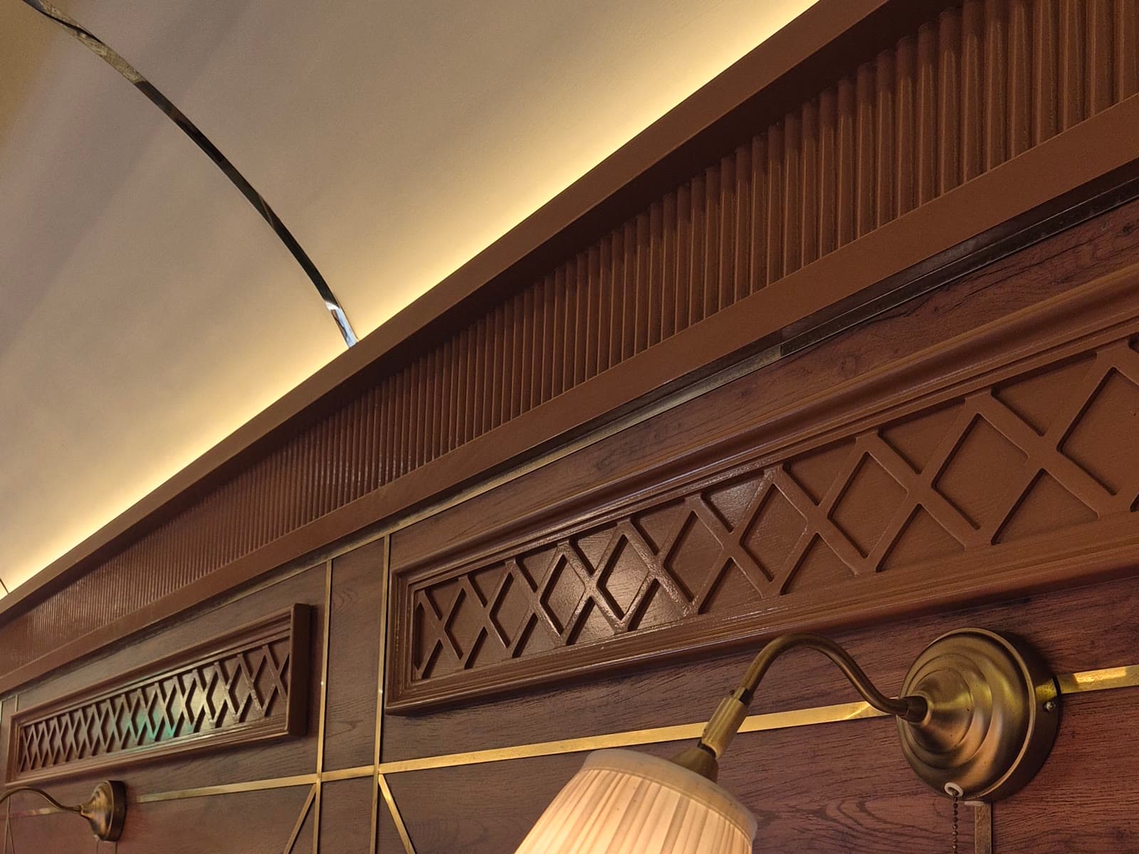Dark wood wall panelling with lattice detailing, brass trim and concealed cove lighting